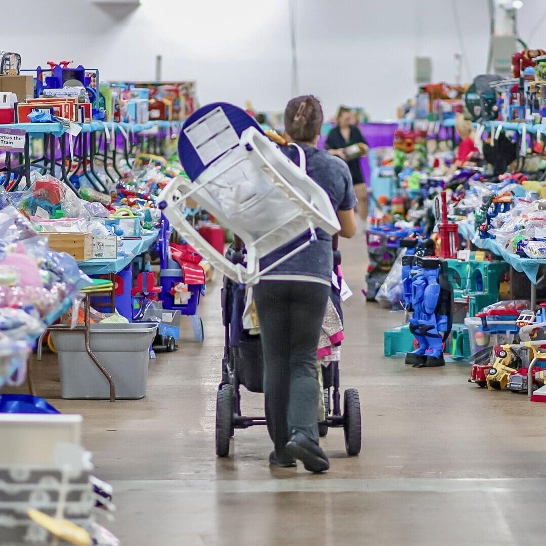 Mother and her two daughters all shopping together. They are all holding baby clothing on hangers.
