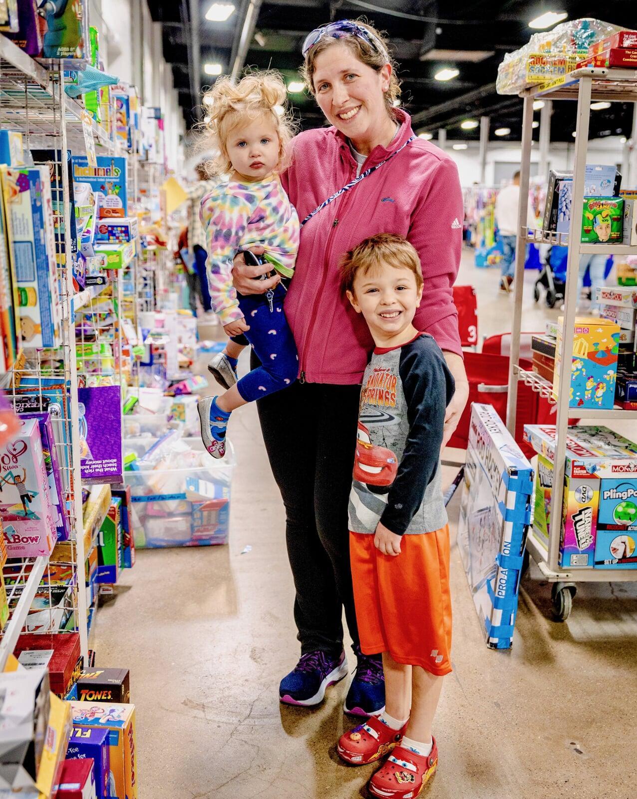Mother shopping with her two children. She is holding one child and has her arm around her other child.