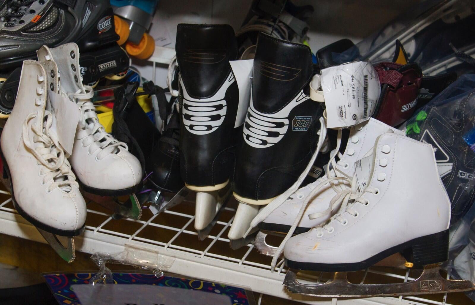 One pair of black ice skates and two pair of white ice skates on white metal shelf.