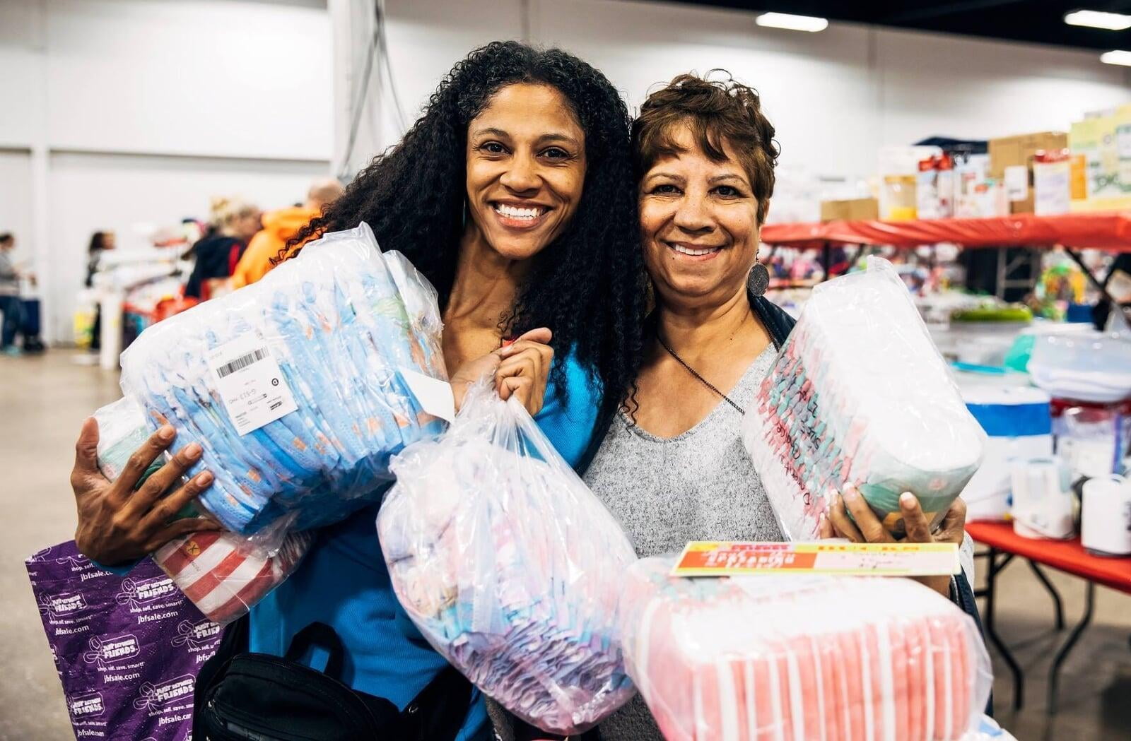 Two women shopping are holding packs of diapers.