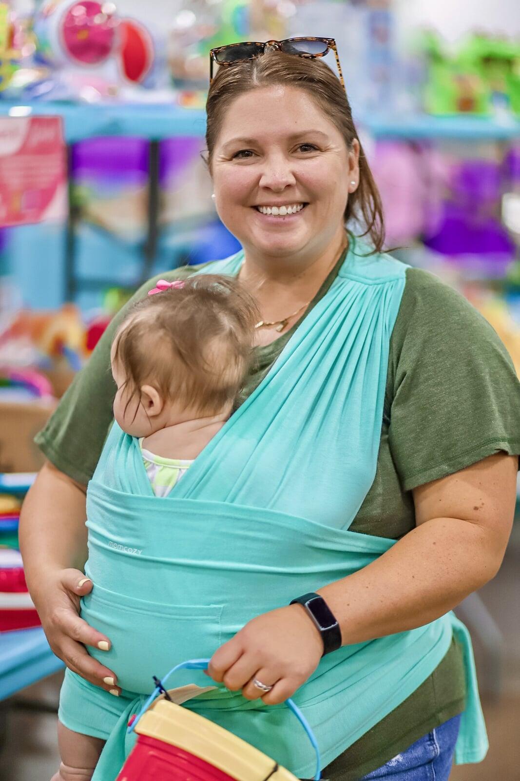 A mom, grandmother and grandfather are shopping with their daughter/granddaughter. The little girl is in a stroller and the adults are standing behind her, all holding up clothing for her.