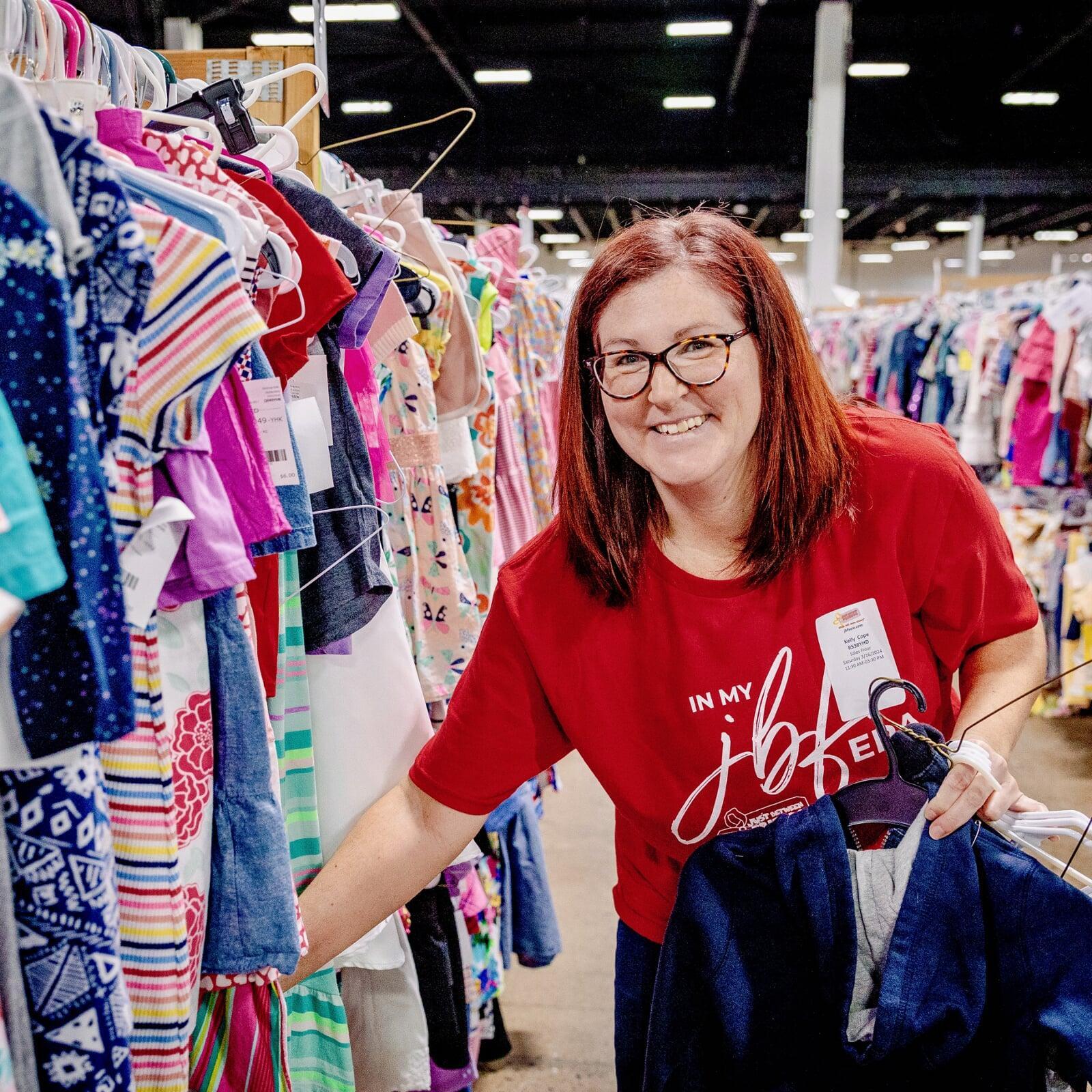 A JBF Team Member smiles as she returns girls clothing to the racks.