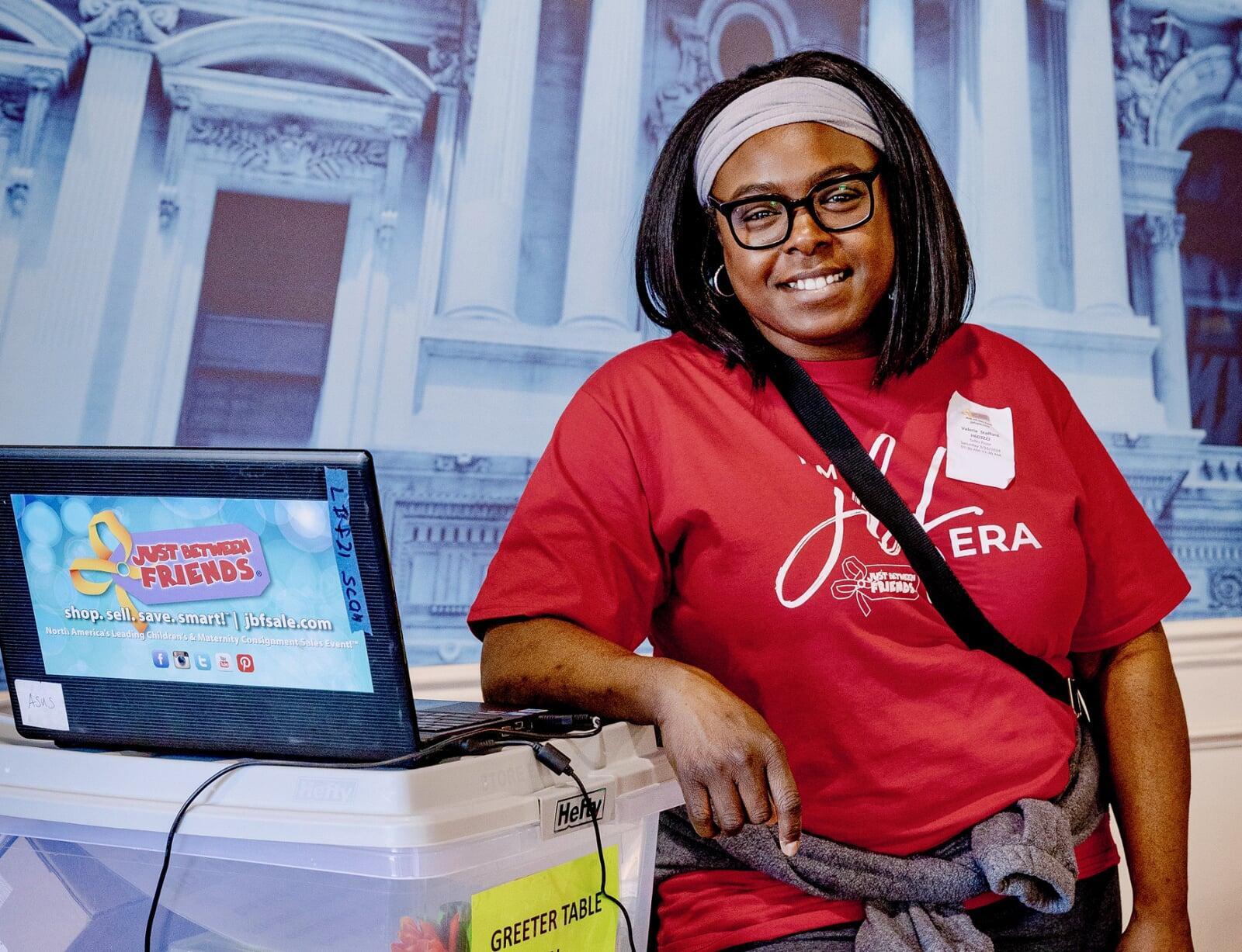 A smiling JBF team member stands at the greeter table ready to welcome JBF shoppers