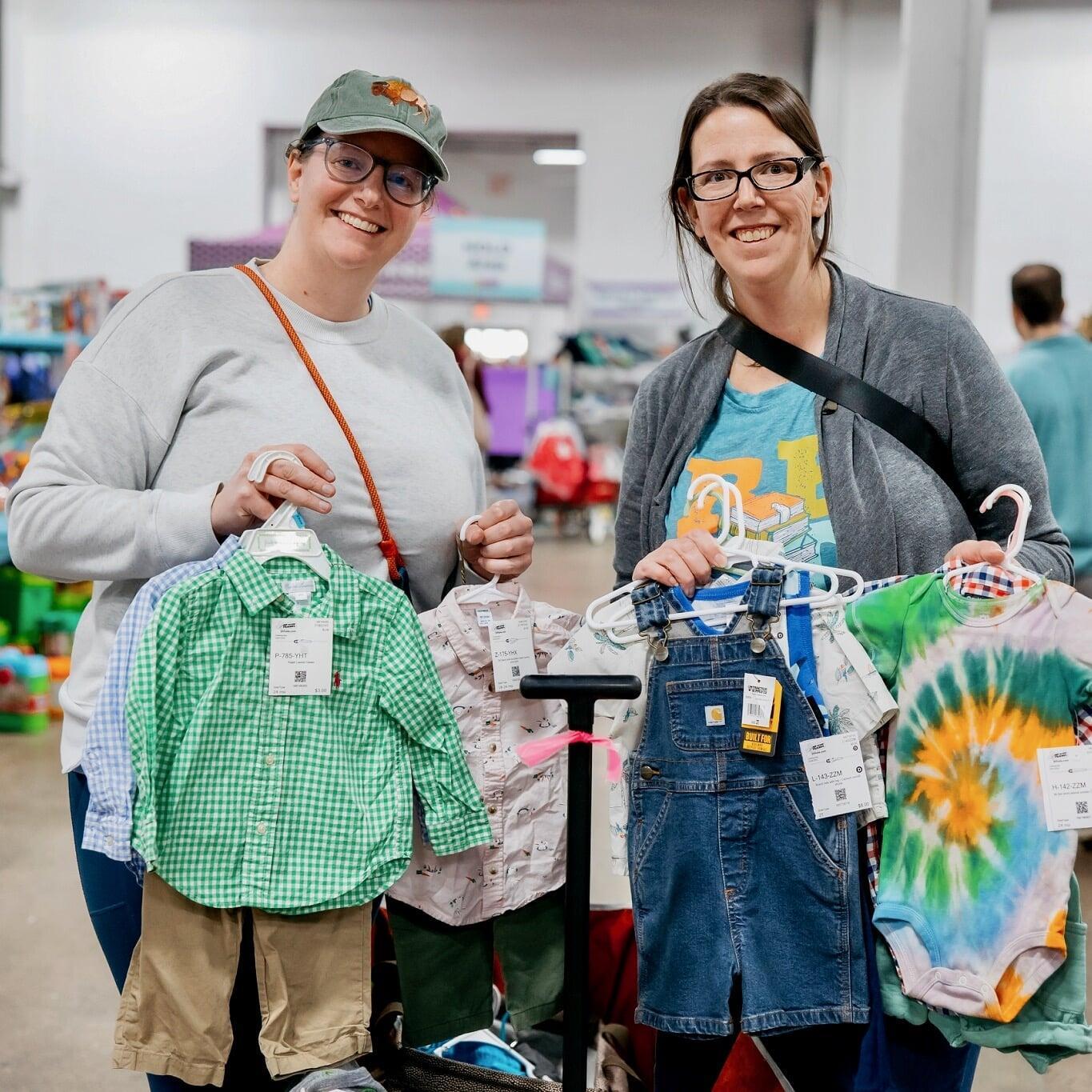 Two women smiling and holding up clothing