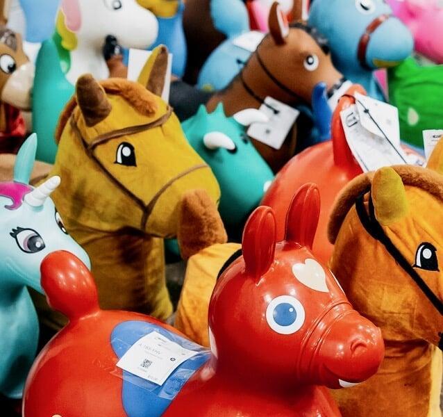 Two women shopping together. One is holding up a sleeveless dress with strawberries on it. The other woman is holding a pair of girls sandals.