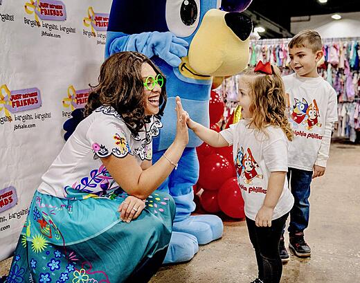 Mirabel Madrigal gives a hight five to a young girl while Bluey stands next to her. A young boy waits for his turn to meet the characters.